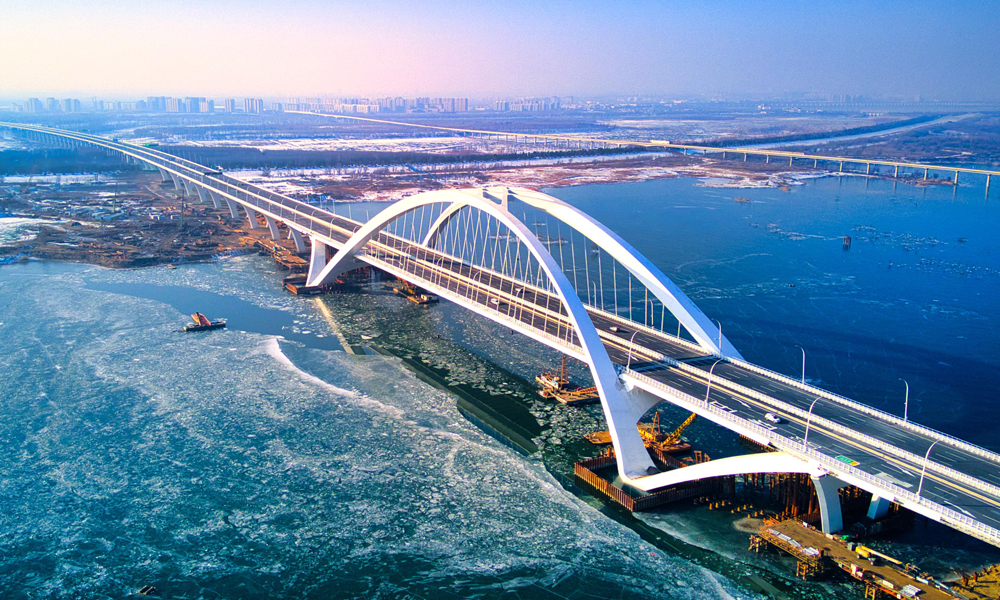 京雄高速公路（北京段）自2020年12月开工建设以来，中国中铁建设者综合利用30余项专利技术优势，先后攻克“筑造精品工程、建设周期保障、危大工程管控、征拆难点破解、关键技术攻坚”五大重难点。全长1.62公里的京雄大桥是国内首座空间异形拱肋飞燕提篮式钢箱拱桥，是北京地区单跨跨度最大桥梁，通过运用数字化孪生技术，采用异形曲面拱肋数字化加工制造、拱肋吊装支架监测等新技术，极大提升了工程建造品质。房山北站是北京市首座陆地高架桥主线收费站，创新性采用桥梁分幅设计，将快慢车、客货车进行分离式指引通行，将大幅提升通行效率。图为京雄高速公路京雄大桥。